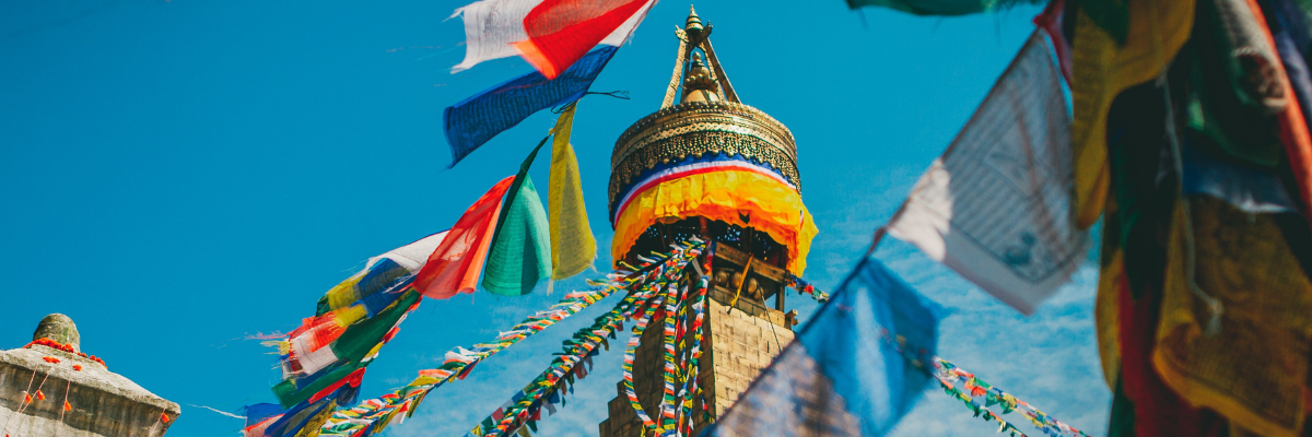 Buddhistische Gebetsfahnen vor einem Stupa und blauem Himmel